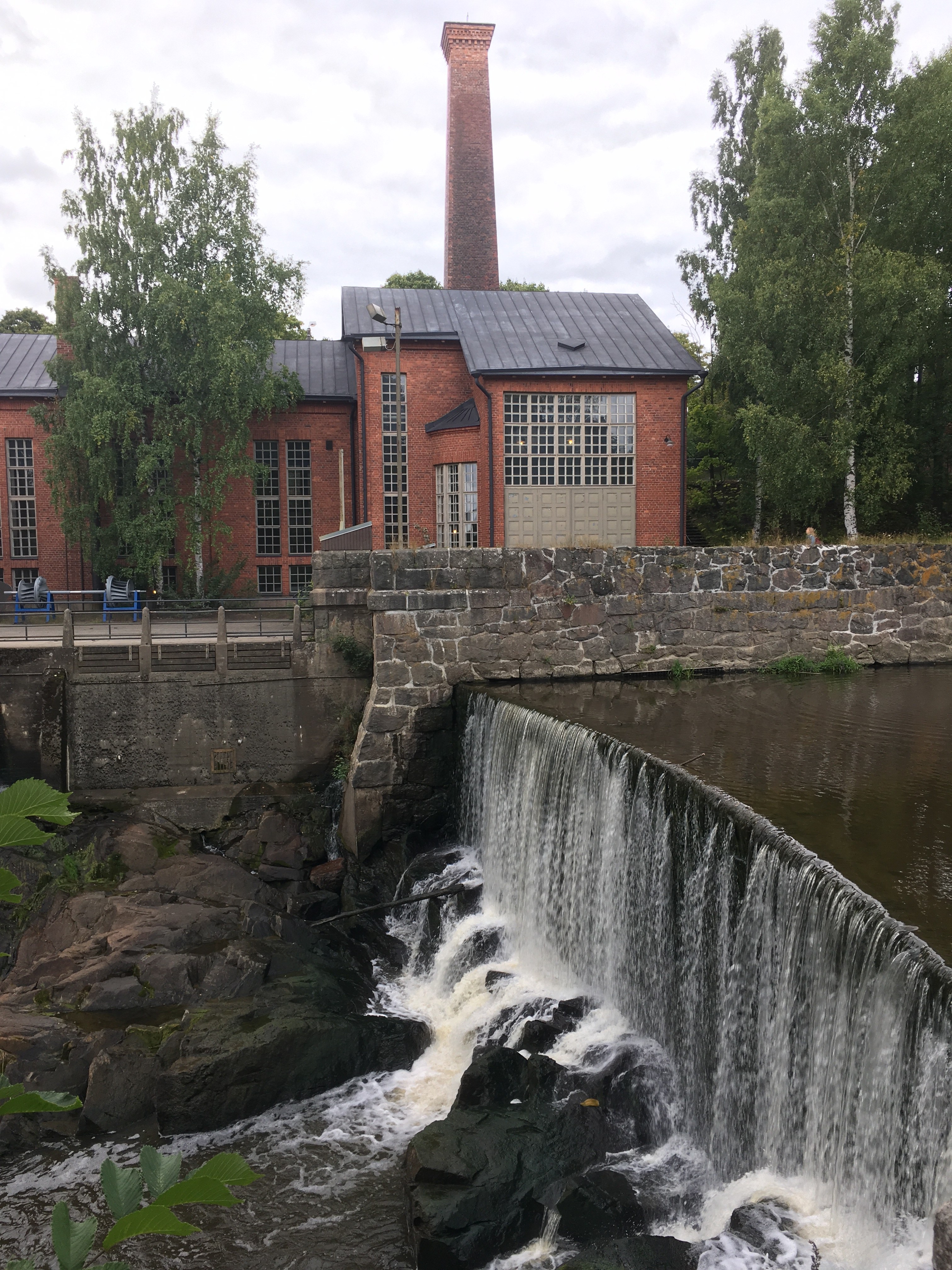 Arkistokuva: Tiilirakennus korkeine savupiippuineen seisoo joen rannalla, jossa vesi virtaa padon yli ja alas kivisiä portaita.