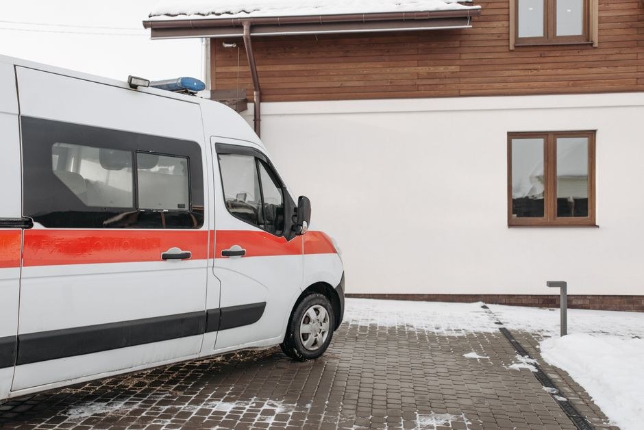 Arkistokuva: Valkoinen ambulanssi punaisella raidalla on pysäköitynä kivetyllä piha-alueella rakennuksen vieressä lumisessa maisemassa.