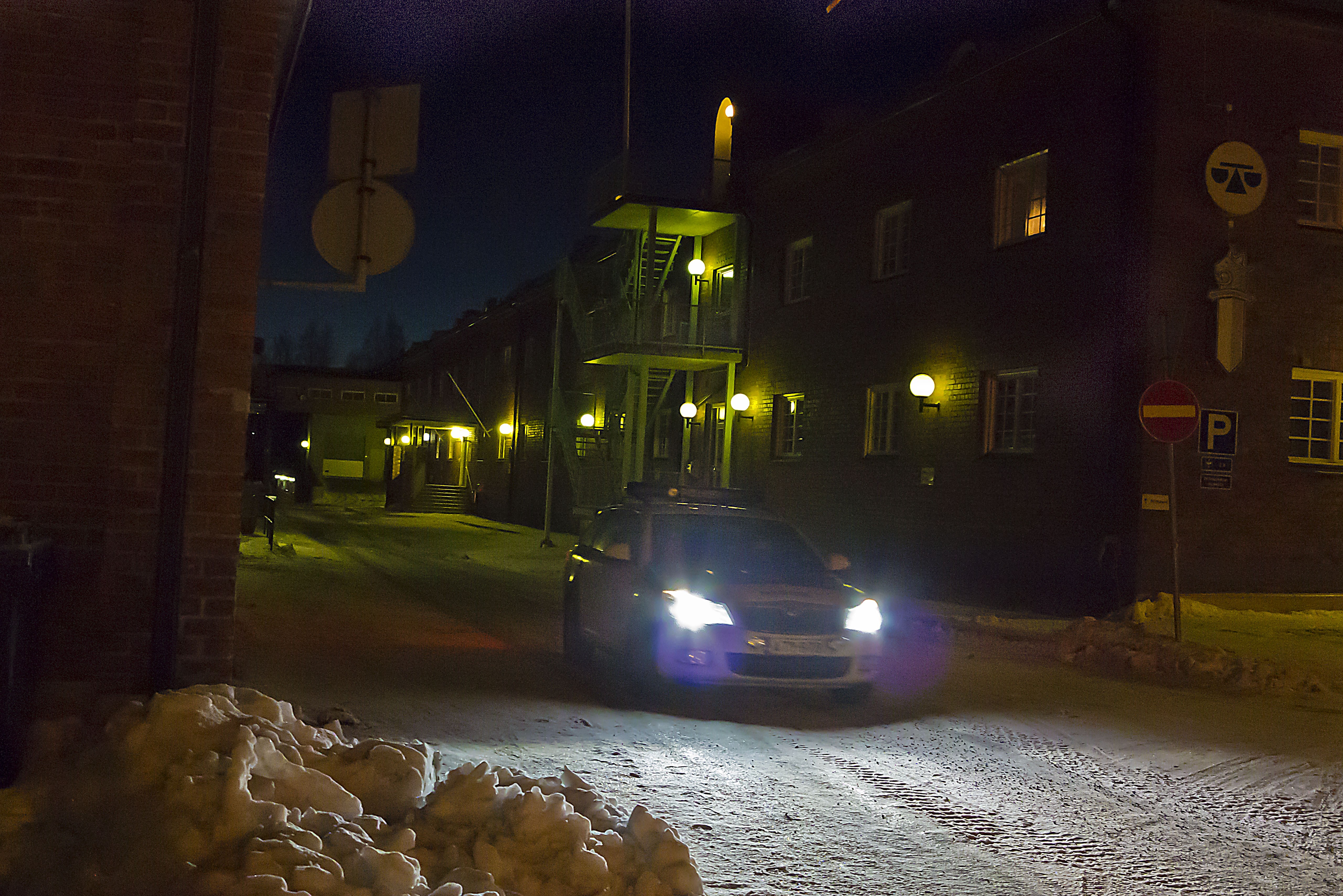 Arkistokuva: Poliisiauto ajaa lumisella kadulla yöllä, rakennusten seinillä on valaisimia ja taustalla näkyy portaikko.