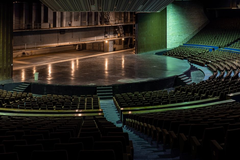 Arkistokuva: Laaja näkymä tyhjästä auditoriosta, jossa tummat istuinrivit kaartuvat suuren, tumman lavan ympärille.
