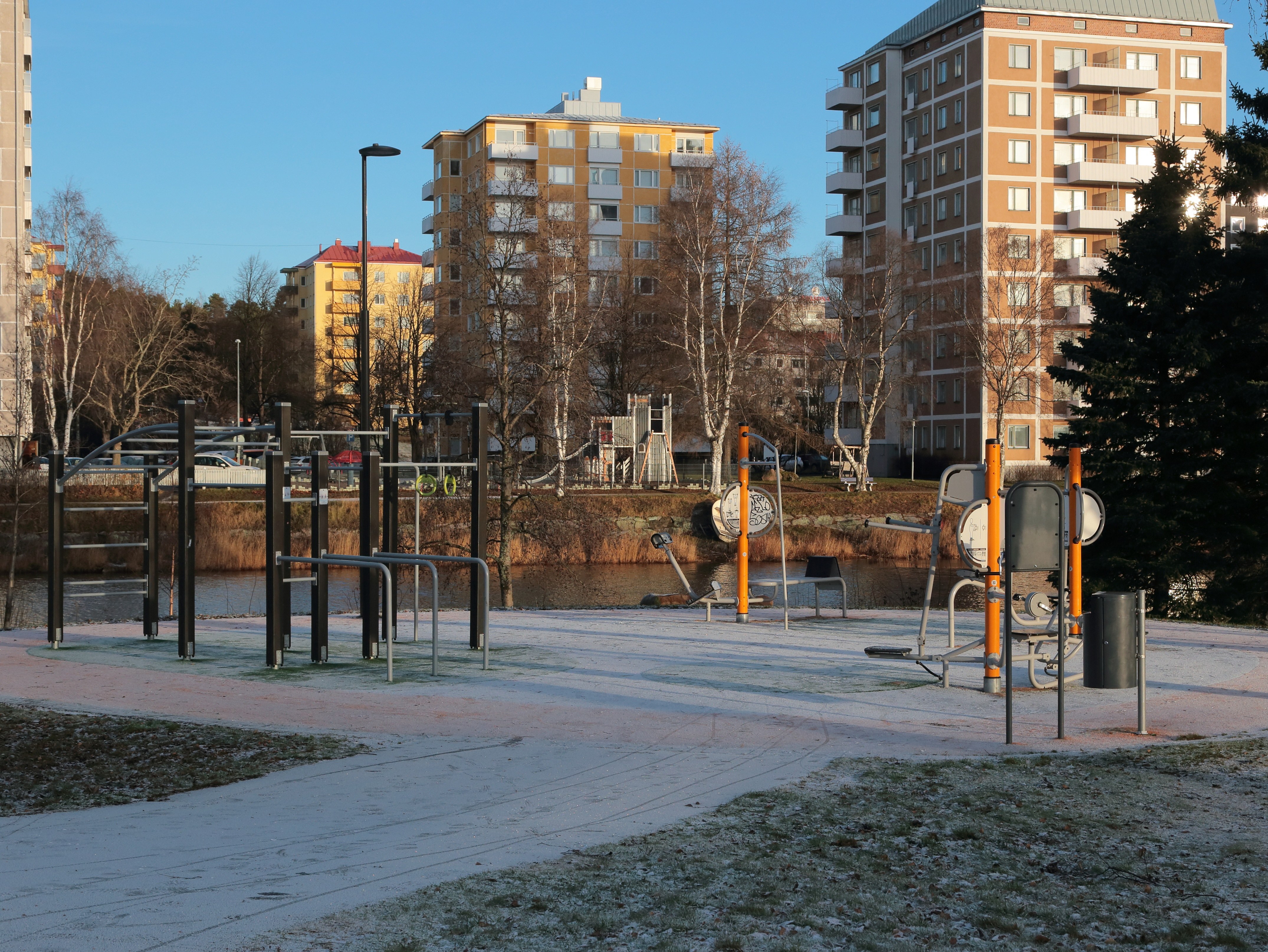 Arkistokuva: Ulkoliikuntapaikalla on useita kiinteitä kuntoilulaitteita, jotka ovat kevyen lumipeitteen alla asuinrakennusten edustalla.