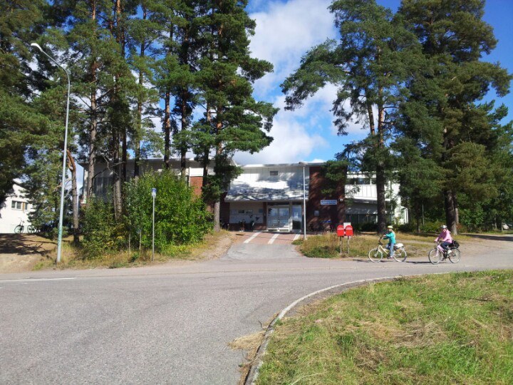 Arkistokuva: Kaksikerroksinen rakennus, jossa on tiili- ja vaaleita julkisivuosia, näkyy osittain puiden takaa tien toiselta puolelta.