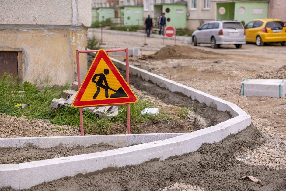 Arkistokuva: Keltainen tietyömerkki ja vaaleat reunakivet sorapohjaisella työmaa-alueella.