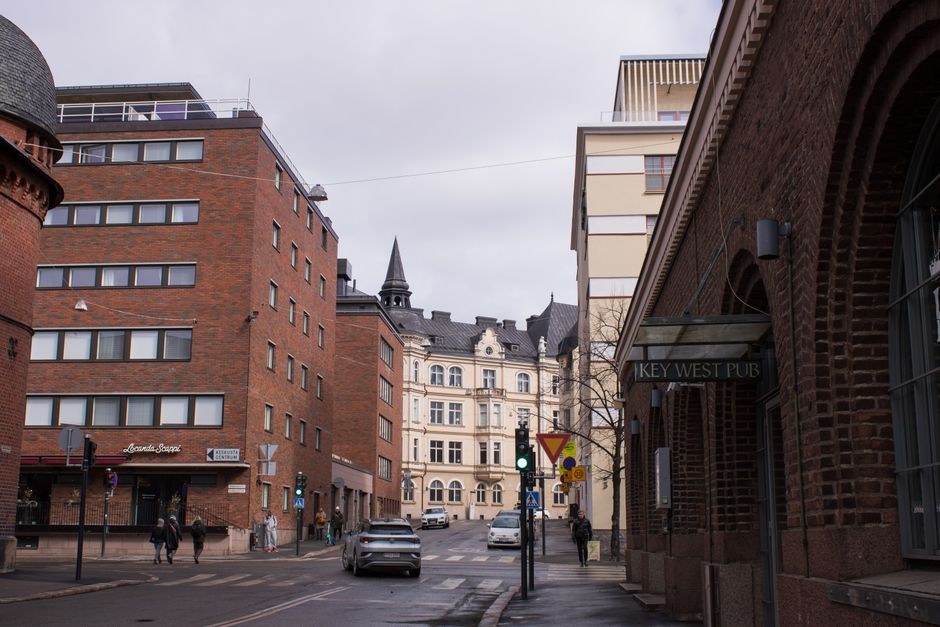Arkistokuva: Katunäkymä kaupungissa, jossa on useita tiili- ja vaaleafasadisia kerrostaloja, autoja ja jalankulkijoita jalkakäytävillä.