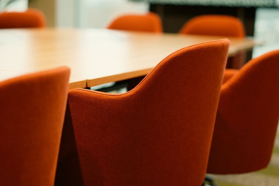 Arkistokuva: Useita oransseja verhoiltuja tuoleja on aseteltu vaalean puisen pöydän ympärille tyhjässä kokoushuoneessa.