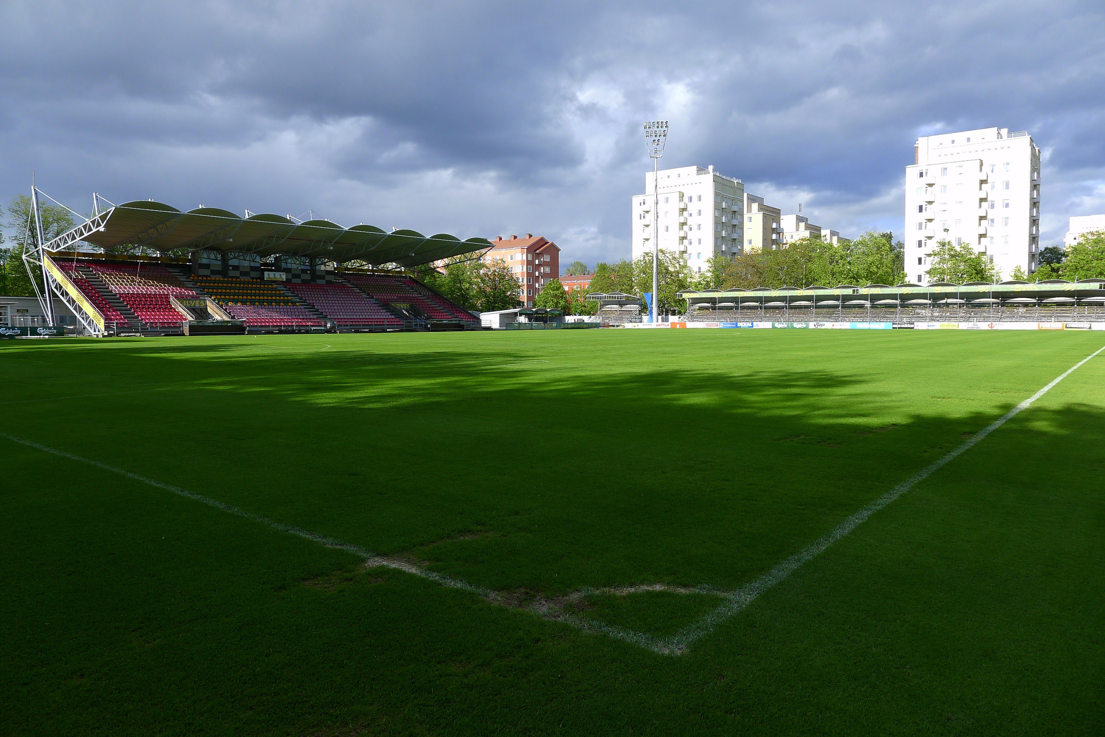 Arkistokuva: Jalkapallostadionin vihreä nurmikenttä ja katsomorakenteet näkyvät pilvisenä päivänä, taustalla kerrostaloja.
