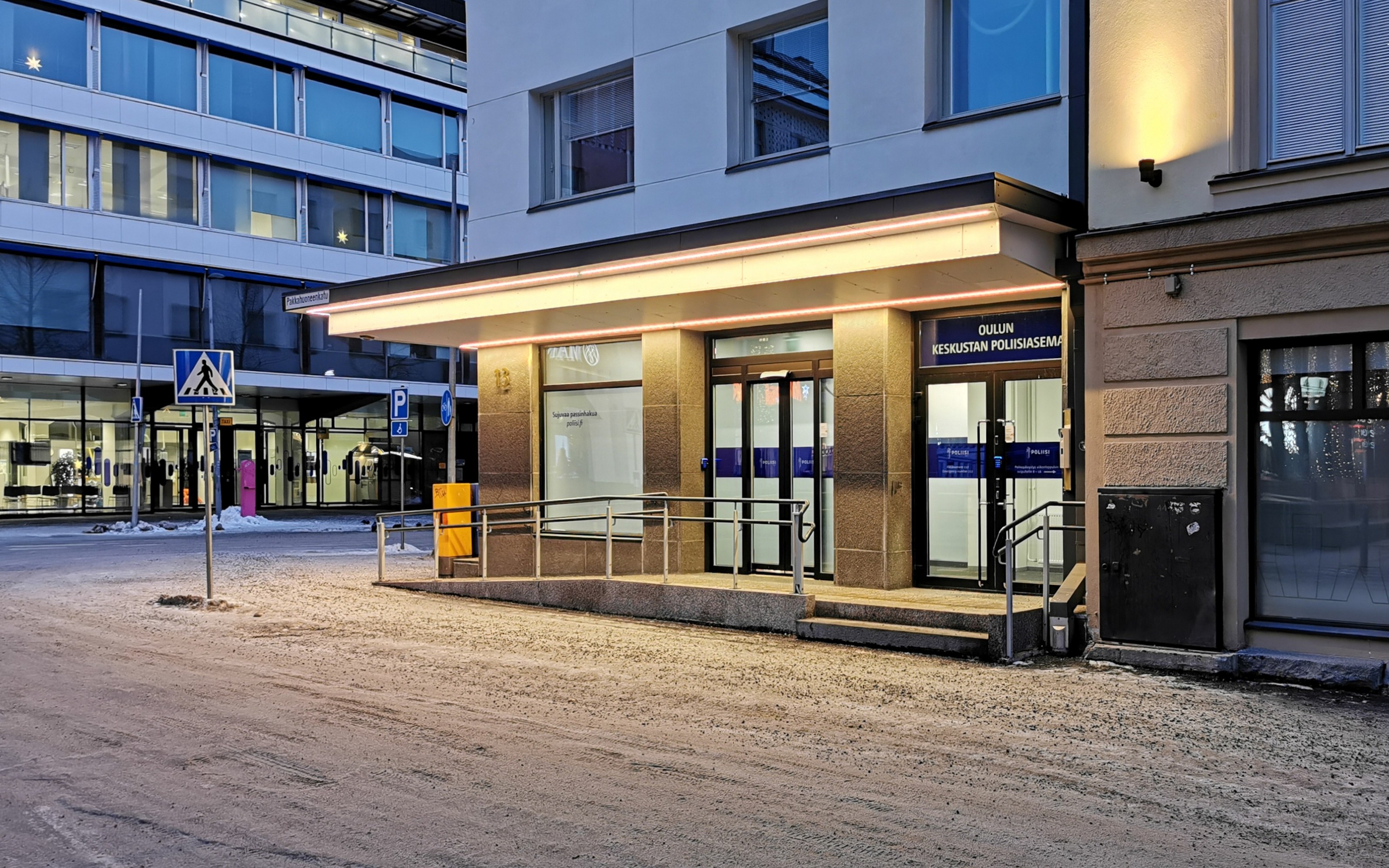 Arkistokuva: Oulun Keskustan Poliisiaseman sisäänkäynti, jossa on lasiovet, valaistu katos ja luiska kaiteineen. Maassa on ohut kerros lunta.