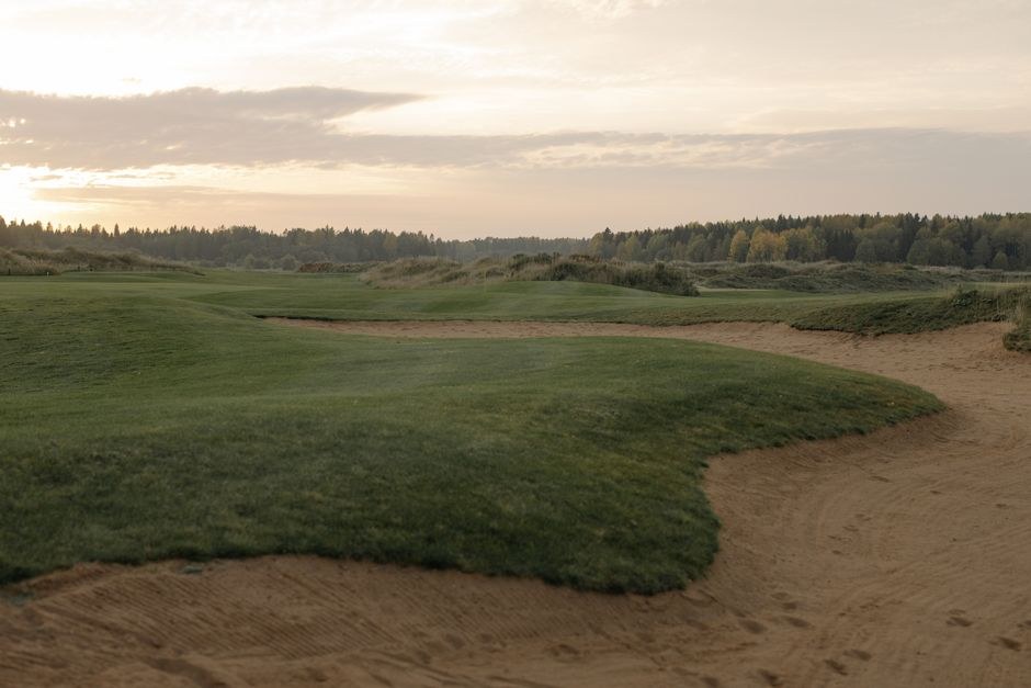 Arkistokuva: Golfkenttä, jossa on vihreitä nurmialueita ja hiekkabunkkereita pilvisen taivaan alla. Taustalla näkyy metsänreuna.