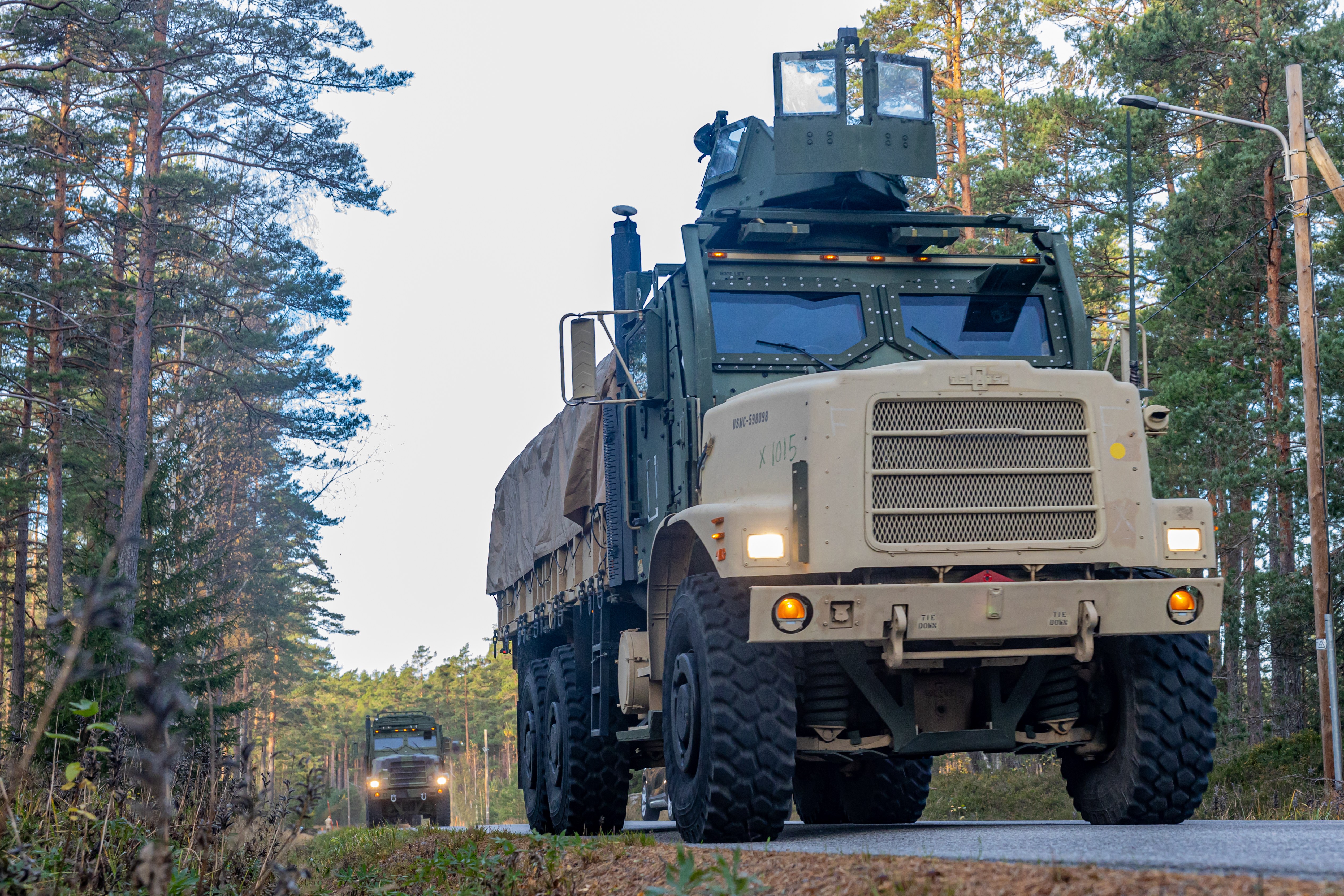Arkistokuva: Maastonvihreiden ja hiekanväristen sotilasajoneuvojen saattue ajaa kaksikaistaisella asfalttitiellä metsän keskellä kirkkaana päivänä.